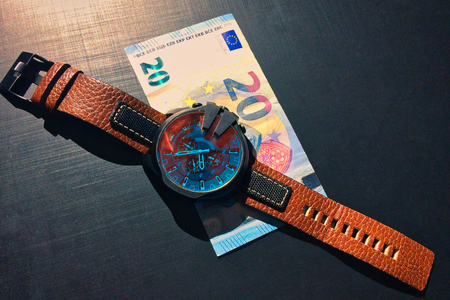 wrist watch with leather strap near the banknote on a dark background, watch on top of money, time is money, wristwatch, European currency, twenty eurosの写真素材