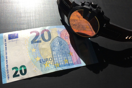 wrist watch with leather strap near the banknote on a dark background, watch on top of money, time is money, wristwatch, European currency, twenty eurosの写真素材