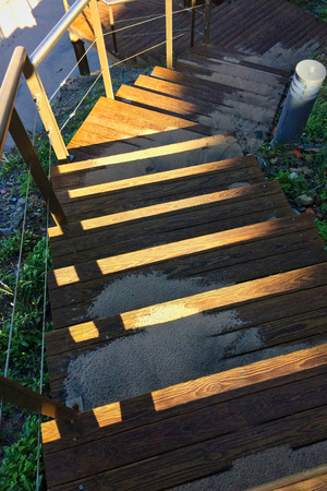 steep wooden staircase leading down, sand scattered on the steps, the sun's rays play on the woodの写真素材