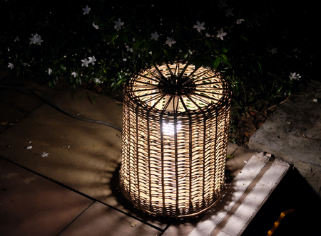 Night lantern woven from a rod. Bush with small white flowers. Night scene