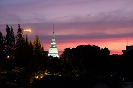 Beautiful sunset over the silhouettes of trees. Lighted spire of a Buddhist temple.の写真素材