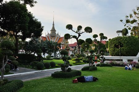 Bangkok, Thailand, December 26, 2018. Several people are resting on the lawn in the garden in front of a Buddhist temple.のeditorial素材
