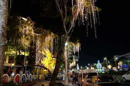 Bangkok, Thailand, December 26, 2018. A tree decorated with garlands grows near the road on which cars drive at night.のeditorial素材