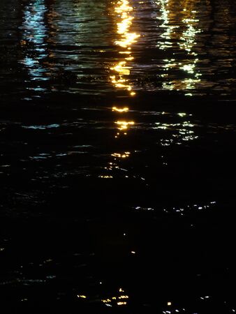 City lights reflect in the waters of the river at night. Background.