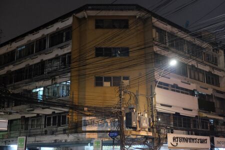 Bangkok, Thailand, December 28, 2018. Plexus wires of power lines. An ugly modern building in a night city.のeditorial素材