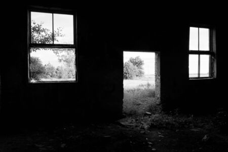 Two broken windows and an empty doorway in the wall of an abandoned building.の写真素材