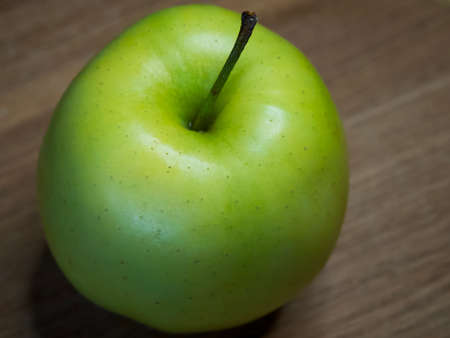 The Reinette Simirenko is an antique apple variety. The fruit has tender, crisp, greenish white flesh with a subacid flavor. A green apple on a wooden tabletop, close-up.の写真素材