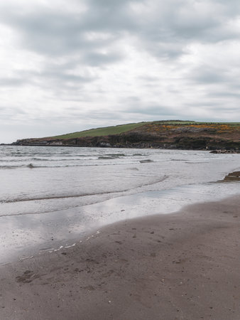 View of Rosscarbery pier from Warren Beach, southern coast of Ireland. Waves on a sandy beach. The Atlantic in cloudy weather.の写真素材