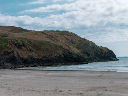 View of the coastal cliffs from the Warren beach. The rocky coast of the south of Ireland. Hills under the sky on a spring day, mountain beside sea under clouds sky.の写真素材