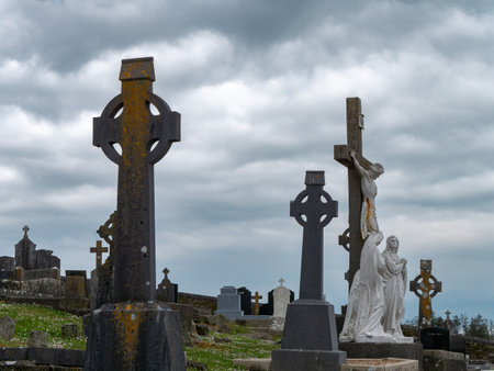 West Cork, Ireland, May 2, 2022. Tombstones in the form of Celtic crosses in an old Catholic cemetery on a cloudy day, cross statue under white clouds.のeditorial素材