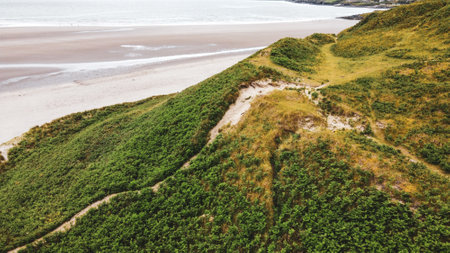 The slope of a high hill on a sandy seashore. Green grass covered mountain beside sea