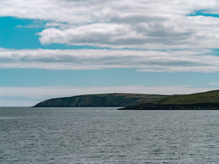 Blue sky with white clouds over the hilly coast of Ireland. Seaside landscape on a sunny day. Body of water near mountains under white clouds and blue skyの写真素材