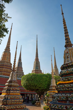 Bangkok, Thailand, December 25, 2018. A Thai temple complex with ornate chedis decorated with gold and colorful tiles under a clear blue sky.のeditorial素材