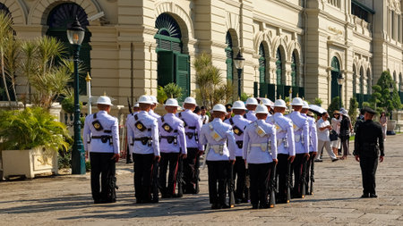 Bangkok, Thailand, December 27, 2018. A group of uniformed men in white helmets and black trousers stand in formation, rifles with bayonets in hand, in front of a white building with green shutters.のeditorial素材
