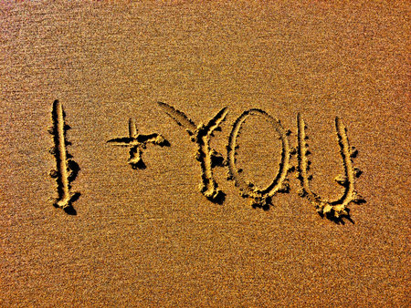 The image displays 'I + YOU' are deeply etched into a sandy surface.の写真素材