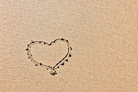 The photo captures a heart outline drawn in sand, highlighting its texture.の写真素材
