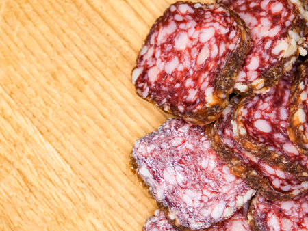 A close up of a wooden table with a pile of meat on it. The meat is sliced and he is salami.の写真素材
