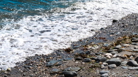 The ocean waves are crashing against the rocks, creating a beautiful and serene scene. The water is a deep blue color, and the rocks are scattered throughout the beach. Scene is peaceful and calming.の写真素材