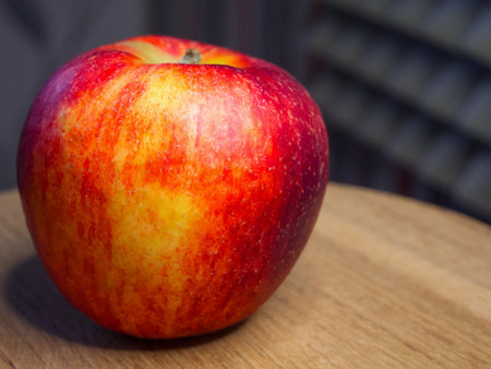 Vibrant red apple, stem intact, water droplets, wooden surface, gray patterned background.の写真素材