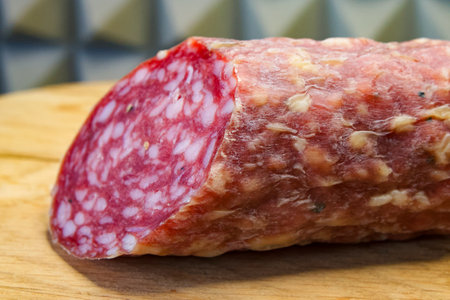 A piece of salami on a wooden board, highlighting its texture and suitability for culinary content.の写真素材