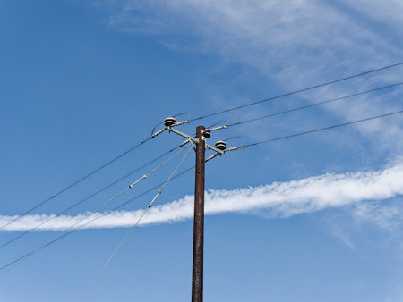 An aged power pole with lines against a blue sky with clouds, symbolizing enduring connectivity.の写真素材