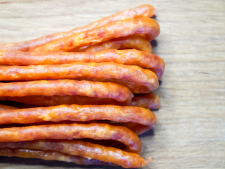 An array of meat sticks lies on a wooden table. They are slender and uniform in color, neatly aligned in a single row, appearing as though they are prepared for consumption.の写真素材