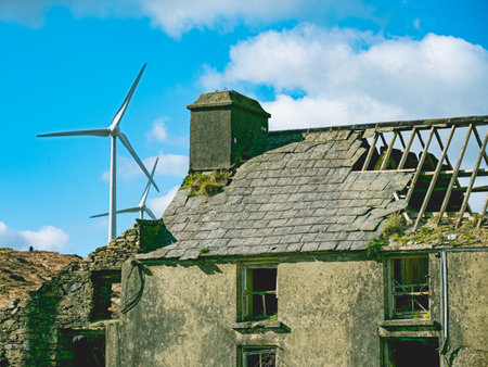 On a clear day in a rural area, an abandoned building with a crumbling roof and wind turbines in the background.の写真素材