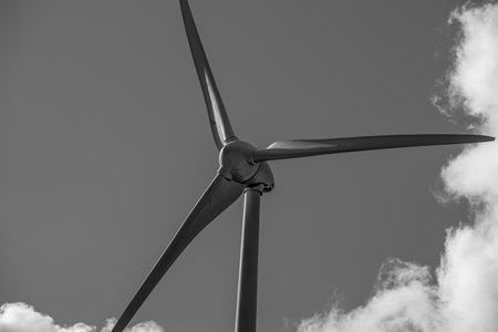 A close-up view of a wind turbine against a vivid sky with scattered clouds during daytime in a renewable energy landscape.の写真素材