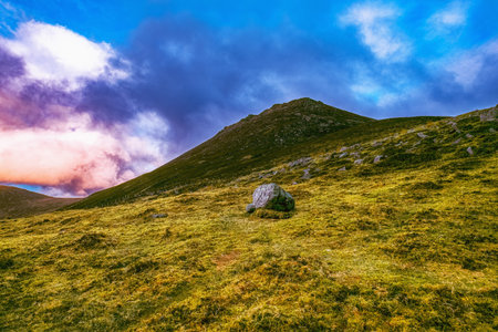 A mountain range with multiple peaks in the distance is partially obscured by clouds. The foreground features a grassy field with scattered rocks.の写真素材