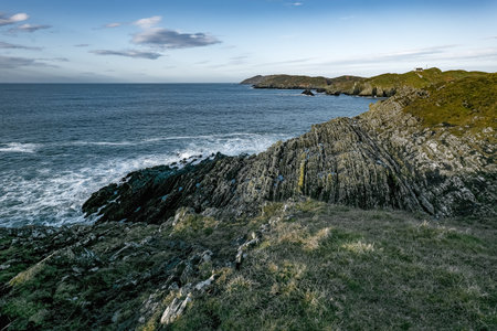 A rocky coastline stretches out into a vast blue ocean. The sky is clear and blue, with a few white...