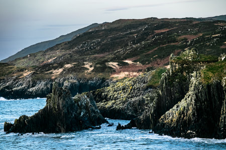 Rugged cliffs rise majestically above the calm blue waters, contrasting with the lush green hills of...