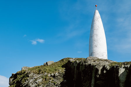 This photo depicts a tall, white, cylindrical structure located on a cliff top overlooking a clear blue expanse of sky.の写真素材