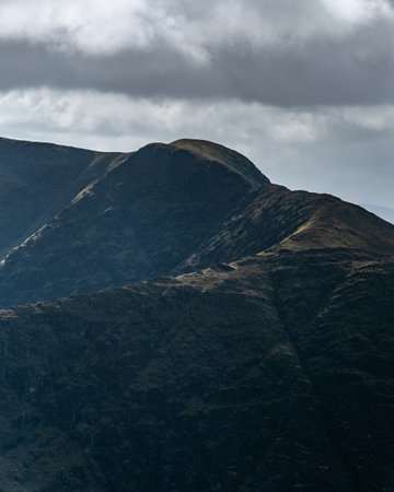 Lush green hills rise dramatically into a cloudy sky. They are bathed in the warm colors of sunset....