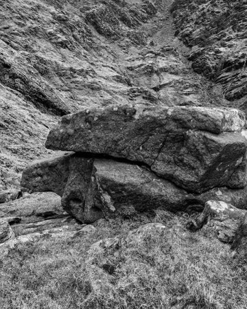 The image shows a large, rugged rock formation in a mountainous area with sparse vegetation and rough terrain.の写真素材