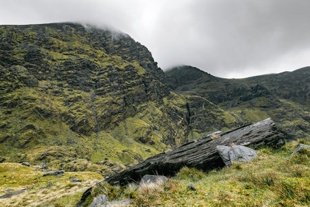 The Carrauntoohil Trail in Ireland is surrounded by lush greenery and towering mountains under a cloudy sky. It captures the natural beauty and atmosphere of the area.の写真素材