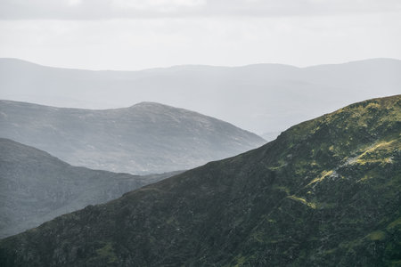 Lush green mountains with varying shades create a captivating view under a gentle cloudy sky. The landscape reveals a peaceful and tranquil environment, inviting exploration.の写真素材