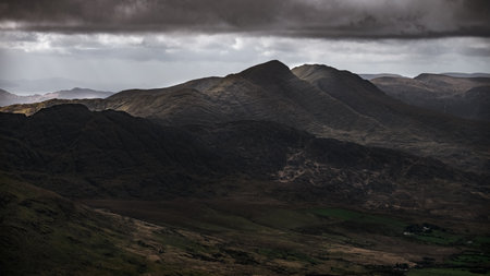 The rugged landscape features steep mountains and deep valleys, surrounded by ominous clouds that hint at changing weather. The view captures the essence of nature's raw beauty.の写真素材