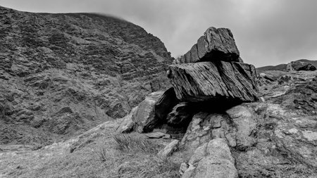 A massive boulder is situated in a rocky landscape, surrounded by uneven ground and steep slopes.の写真素材