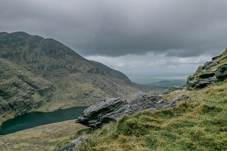 Carrauntoohil walkway, breathtaking views of the surrounding mountains and the serene lake below, all under an overcast sky.の写真素材