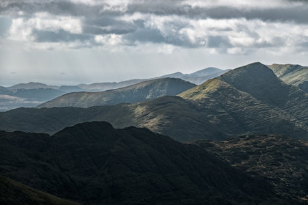 The image shows a detailed view of a mountain range. Varied shades of dark greens and grays indicate different rock formations and vegetation. The sky is overcast.の写真素材
