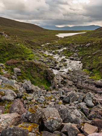 The river flows gently through a rocky terrain in the heart of Ireland, surrounded by lush greenery and distant mountains under a moody sky.の写真素材
