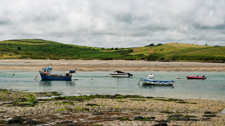 Explore Middle Ring Bay beach in Ireland with boats anchored in the bay under a cloudy sky.の写真素材