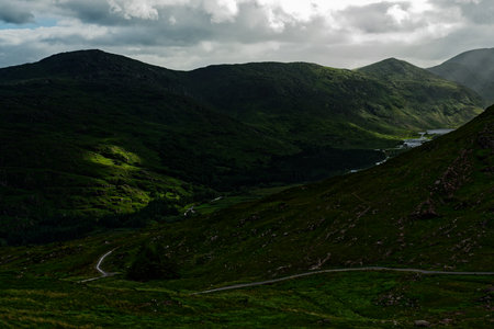 A picturesque Irish countryside scene unfolds, showcasing lush green hills and a meandering road, perfect for a scenic drive.の写真素材