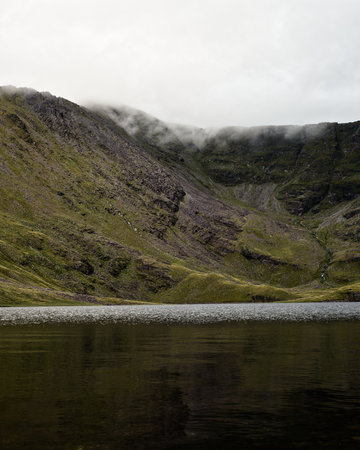 Serene mountain lake framed by imposing cliffs and misty peaks, a breathtaking landscape of contrasts.の写真素材