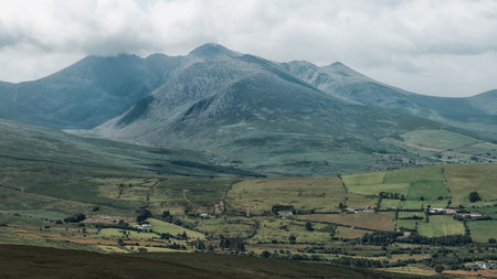 Mountain under cloudy skies with a valley in Ireland, showing vast green grass.の写真素材