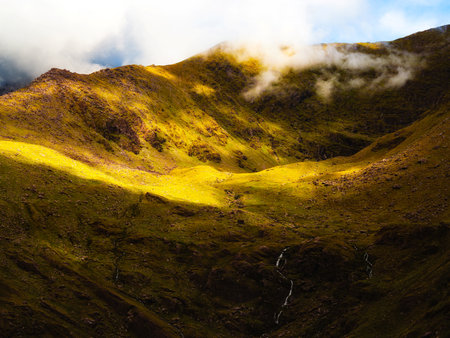 There is a valley in Carrauntoohil that is covered in green plants. There are also a few waterfalls on the rock face, and foggy weather on the mountain tops in County Kerry.の写真素材