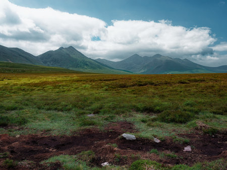 View of Mountain landscape across a verdant grassy field under a blue sky with fluffy clouds in County Kerry, Ireland.の写真素材