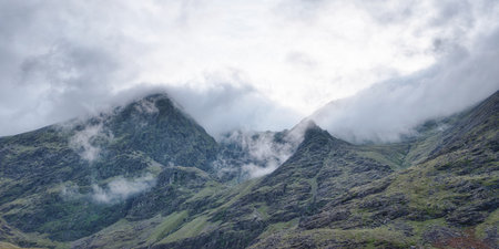 The photograph shows a mountain's rocky face. Small waterfalls cut through the terrain. Clouds partially cover the higher elevations of the mountain.の写真素材