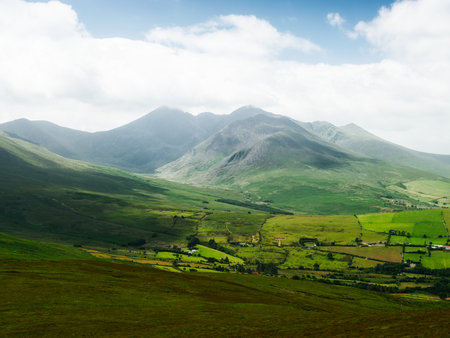 You can see the mountain and the valley it is in, all in Ireland. The landscape is made up of green grass, slopes and mountains, under a cloudy sky.の写真素材