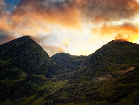 Golden hour illuminates the textured slopes, creating a breathtaking panorama of mountains and sky. A peaceful, vibrant scene.の写真素材